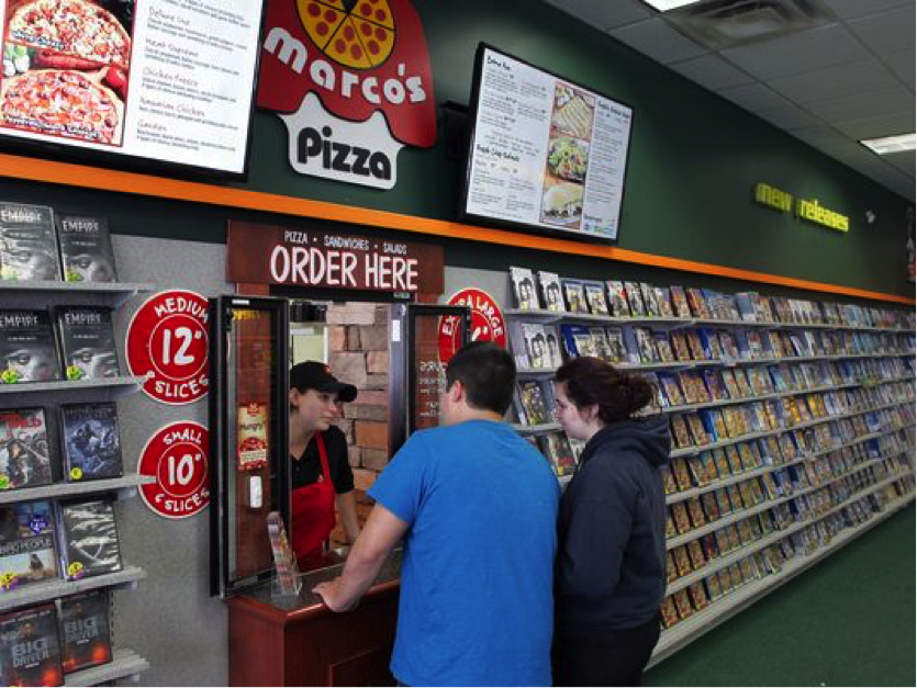 Customers ordering Marco’s Pizza through the pickup window inside Family Video